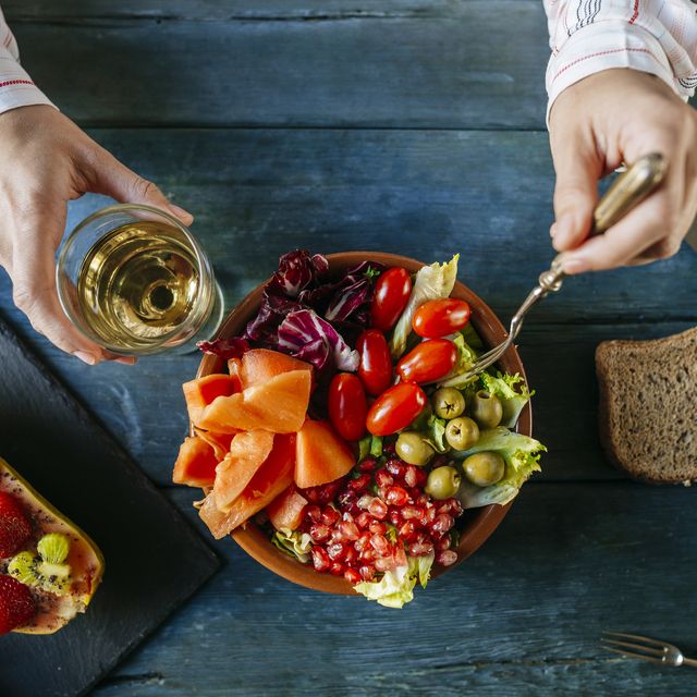 close up of woman's hands eating salad wit tomato, pomegranate, papaya and olives, papaya with fruits and with wine glass