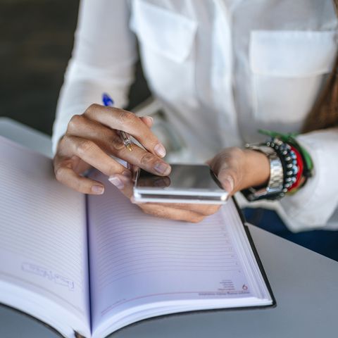 Close-up of woman's hands using a smartphone and a notebook