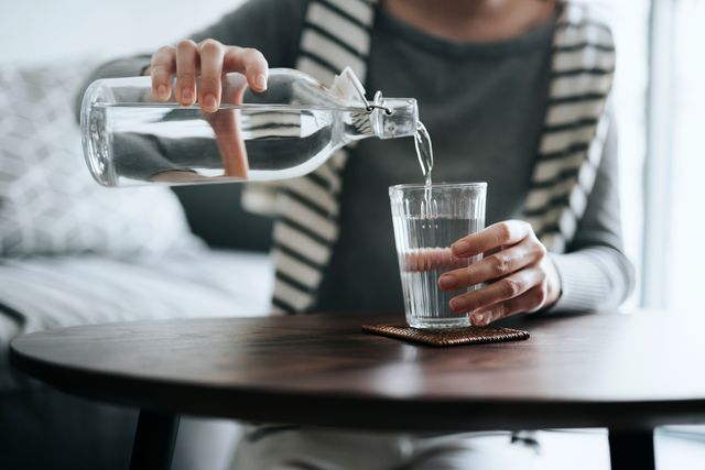 close up of young asian woman pouring water from bottle into the glass on a coffee table at home healthy lifestyle and stay hydrated