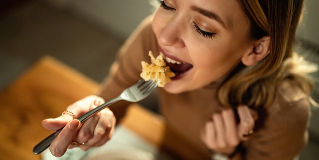 close up of young happy woman eating pasta at dining table