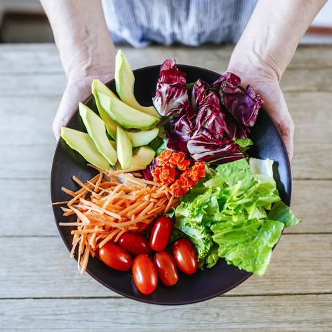 close up salad of avocadolettucetomato and carrot held by woman's hands
