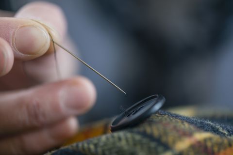 Cerrar los dedos de la costurera botón de coser en tartán en el taller