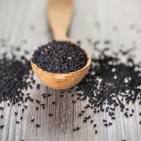 close up shot of dried seeds of black cumin seeds kalinji on wooden spoon on rustic wooden background soft focus