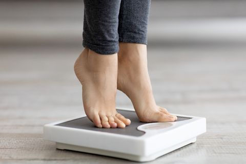 closeup of young indian woman standing on scales, measuring her weight indoors