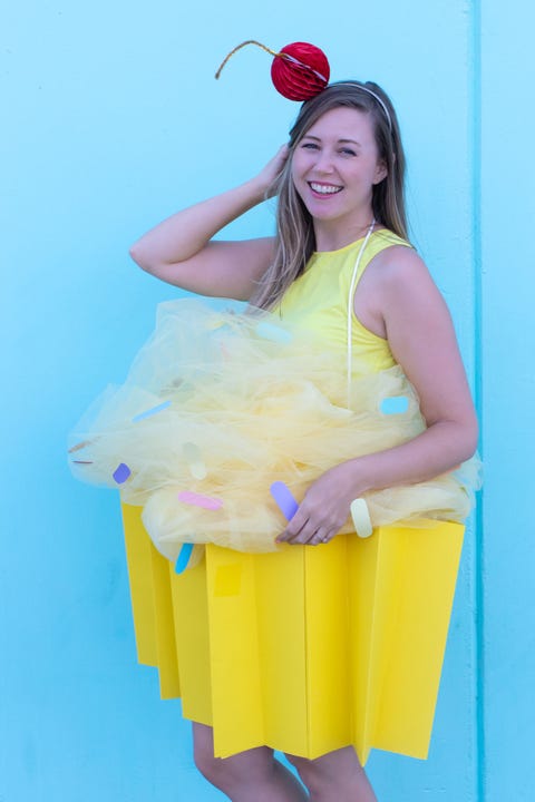 woman dress as cupcake with yellow wrap bottom, pale yellow tulle on top with paper "sprinkles" and a paper red "cherry" on her head