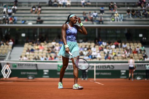 coco gauff smiles and touches her forehead with her left hand as she walks away from the net towards the baseline during a tennis match