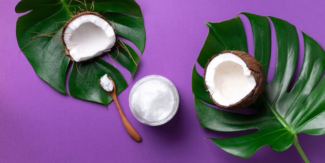 coconut oil and ripe coconuts, tropical palm and monstera leaves on violet background with copy space top view summer creative layout