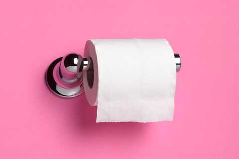 Roll of toilet paper on dispenser in front of pink bathroom wall.