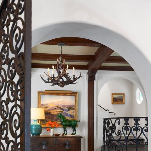 entry type of area with platform to the right that leads upstairs through an archway and beautiful wrought iron heart shaped railings around the platform and on the gate and a soft colored rug on the wood floors