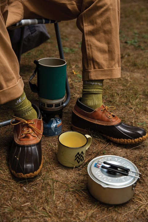 Person wearing rain boots, socks and rolled up pants and holding camping equipment