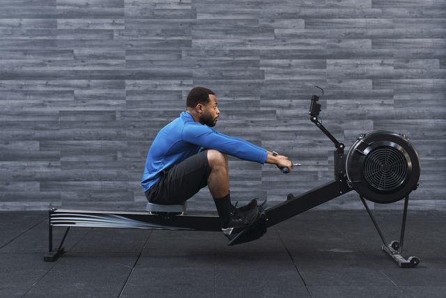 concentrated athlete exercising on rowing machine in front of wall in gym