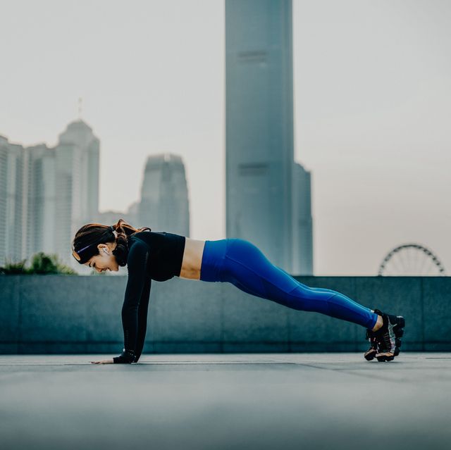 confidence and energetic young asian sports woman exercising and working out outdoors in urban park against city skyline at sunset