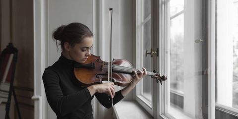 Confident woman with sheet music on window sill playing violin in mansion