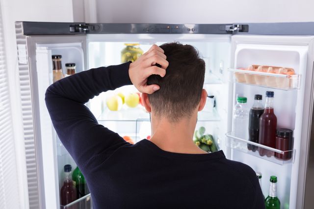 confused man looking at food in refrigerator