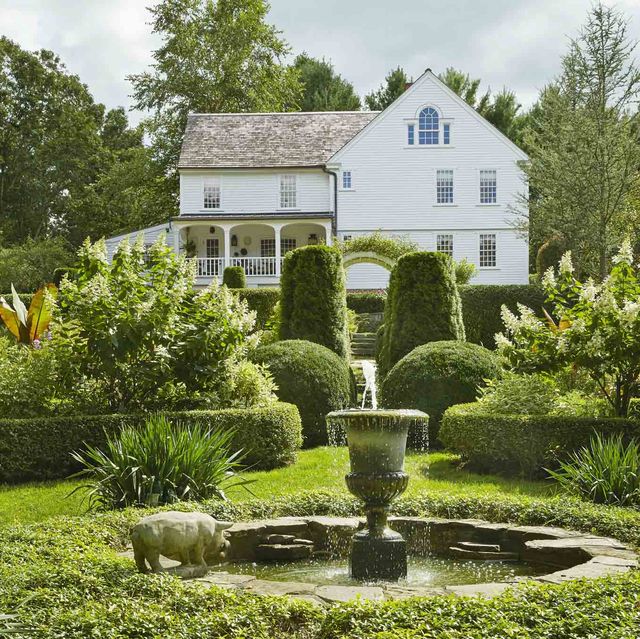 a low privet hedge forms a traditional rondel inside it, a fountain with stone from a mini quarry on the property surrounded by vinca minor ground cover a grand white farmhouse is in the background