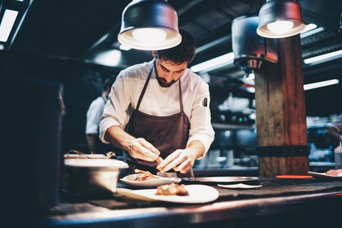 cook serving food on a plate in the kitchen of a restaurant