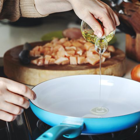 woman pouring olive oil into the skillet preparing for chicken masala dish home cooking
