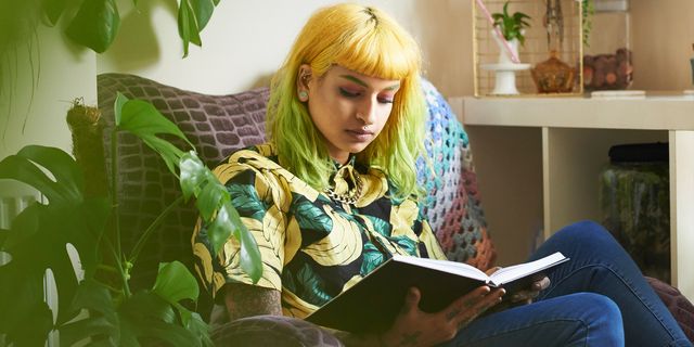 jonge vrouw met geel en groen geverfd haar zit in een stoel een boek te lezen