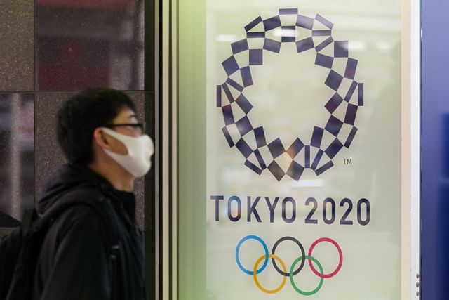 un hombre se protege con mascarilla delante de una imagen oficial de los juegos olímpicos de tokio