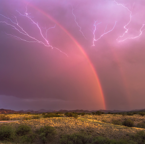 lightning strikes on each side of a rainbow in a field