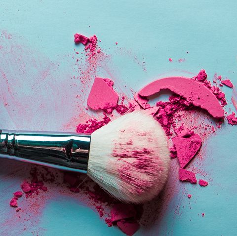 Cosmetic brush and crushed make-up, blush, eye-shadow on blue background