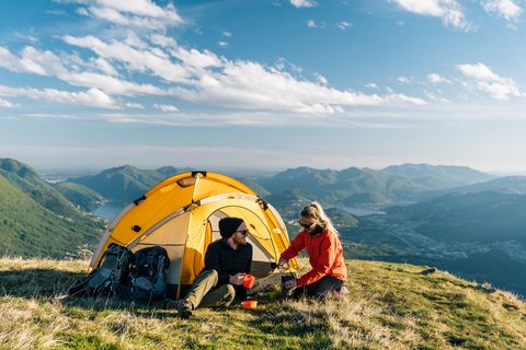 couple camping on mountain top, prepare food and beverages next to tent