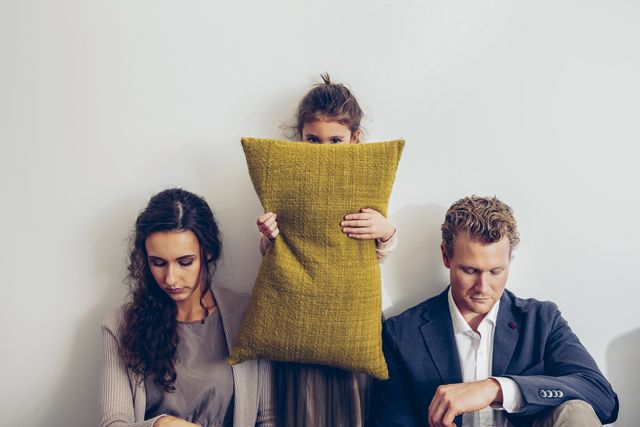 couple having relationship conflict with their daughter hiding her face behind cushion
