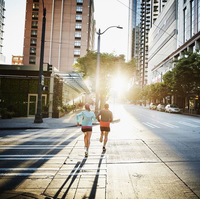 couple running together on empty city street during workout at sunrise