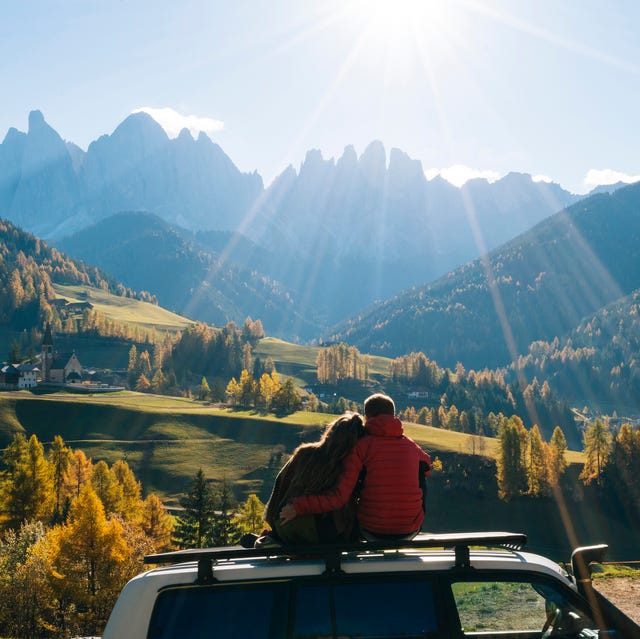Couple sit on car rooftop looking at mountains in the distance couple sit on car rooftop looking at mountains in the distance