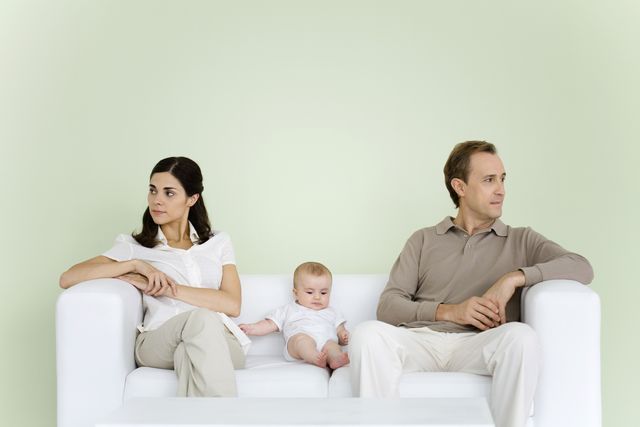 couple sitting on couch with baby between them, both looking away