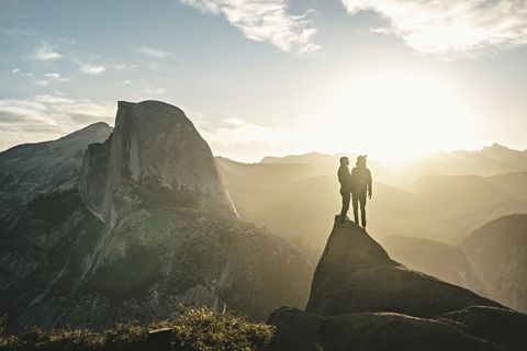couple standing on cliff against mountains on sunny day