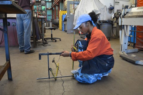 student in orange sweatshirt kneeling while working on art