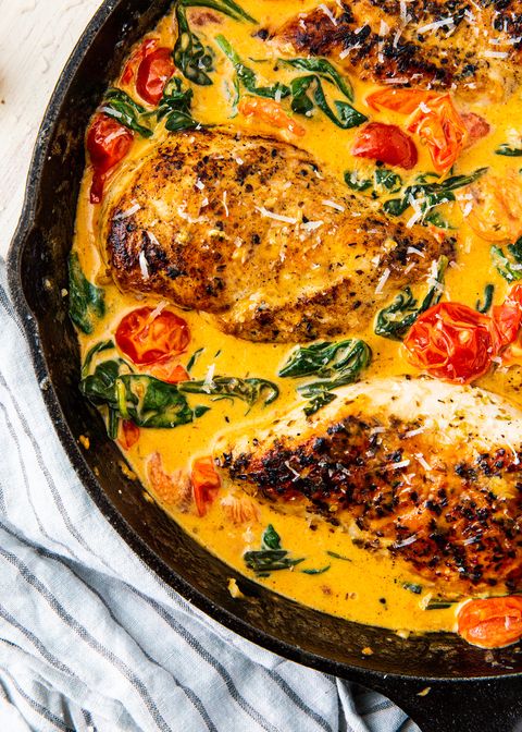 tuscan chicken in a creamy yellow sauce with spinach and baby tomatoes in a black cast iron pan