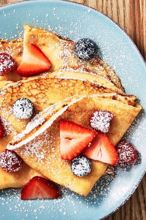 crepes on a plate topped with fruit and powdered sugar