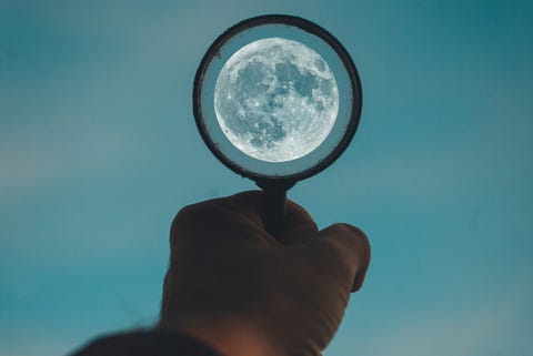 Cropped Hand Holding Magnifying Glass Against Sky