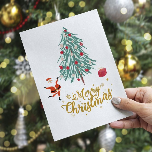 cropped hand of woman holding greeting card against christmas tree