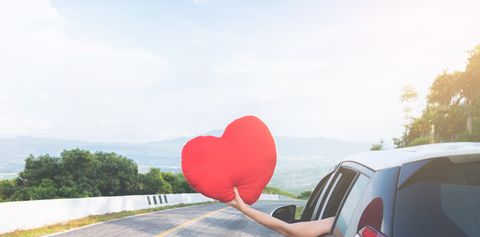 Cropped Hand Of Woman Holding Heart Shape In Car Against Sky