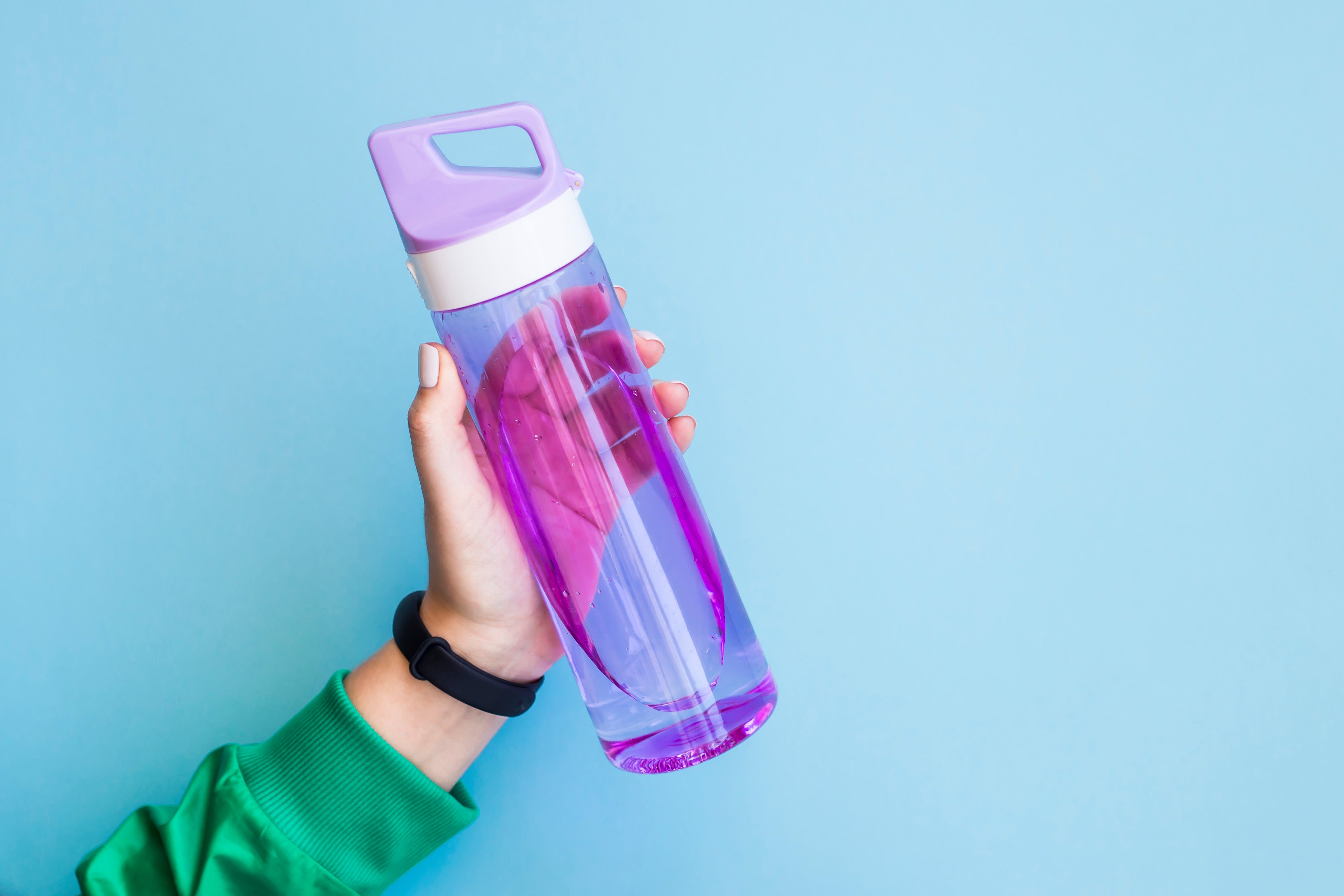  main recadrée de femme tenant une bouteille d'eau violette sur fond bleu