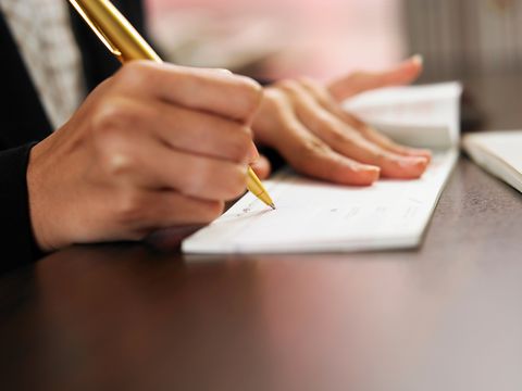 cropped hand of woman signing on check over table