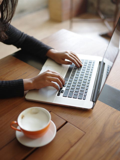 Cropped Hand Of Woman Using Laptop With Coffee On Table