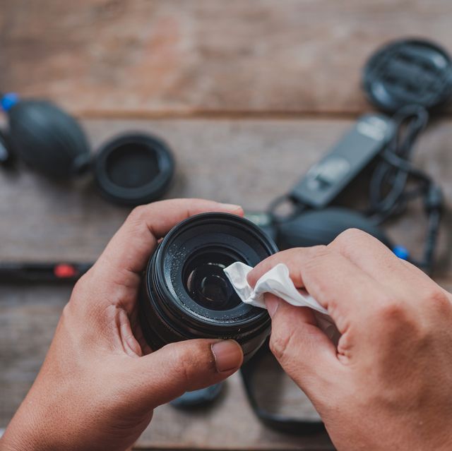 cropped hands of man cleaning camera lens on table