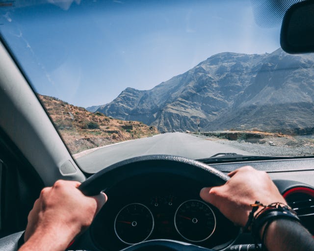 Les mains coupées de l'homme au volant de la voiture sur la route contre le ciel