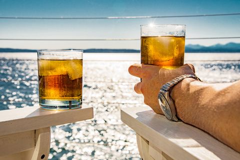 cropped image of man holding rum glass at beach