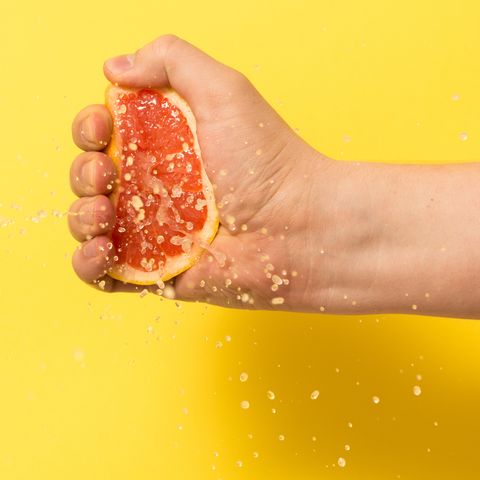 cropped image of person squeezing grapefruit slice against yellow background