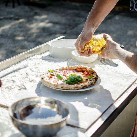 cropped man pouring oil on pizza on plate in back yard