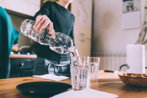 Cropped shot of young woman pouring water at kitchen table