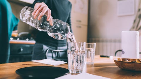 Cropped shot of young woman pouring water at kitchen table Cropped shot of young woman pouring water at kitchen table