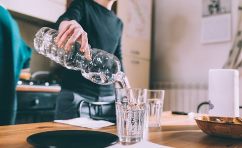 Cropped shot of young woman pouring water at kitchen table