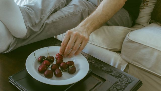cropped view of man reaching into bowl of cherries