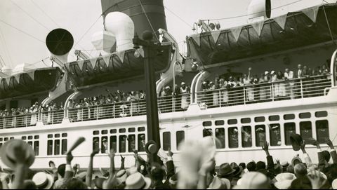 zwartwit foto van menigte die een schip vol mensen uitzwaait